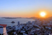Atardecer en Acapulco, mostrando el cielo teñido de colores vibrantes sobre la playa, con personas disfrutando de la vista.